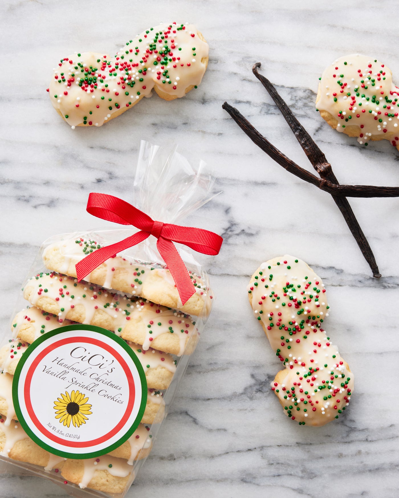 Beautiful and delicious Italian Christmas Vanilla Sprinkle cookies. Dipped in white vanilla icing with red and green nonpareils. laid on white marble surface and window light. Perfect Christmas gift for Italian Americans looking for nostalgia and delicious treats. Packaged with a red bow, they are ready to gift.